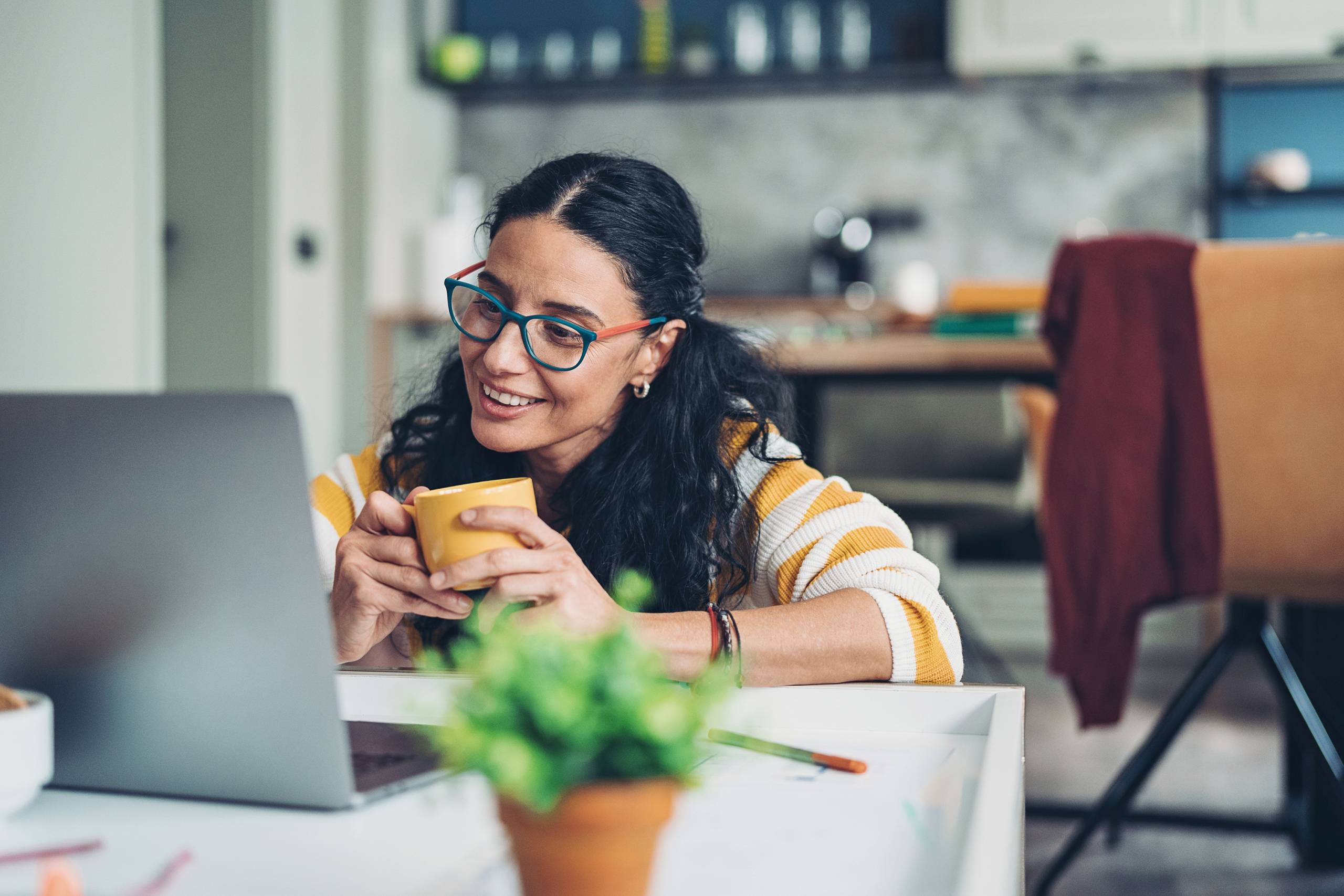 Estudiante sentada y tomando curso en línea en escritorio frente a una laptop con una taza de café en las manos.